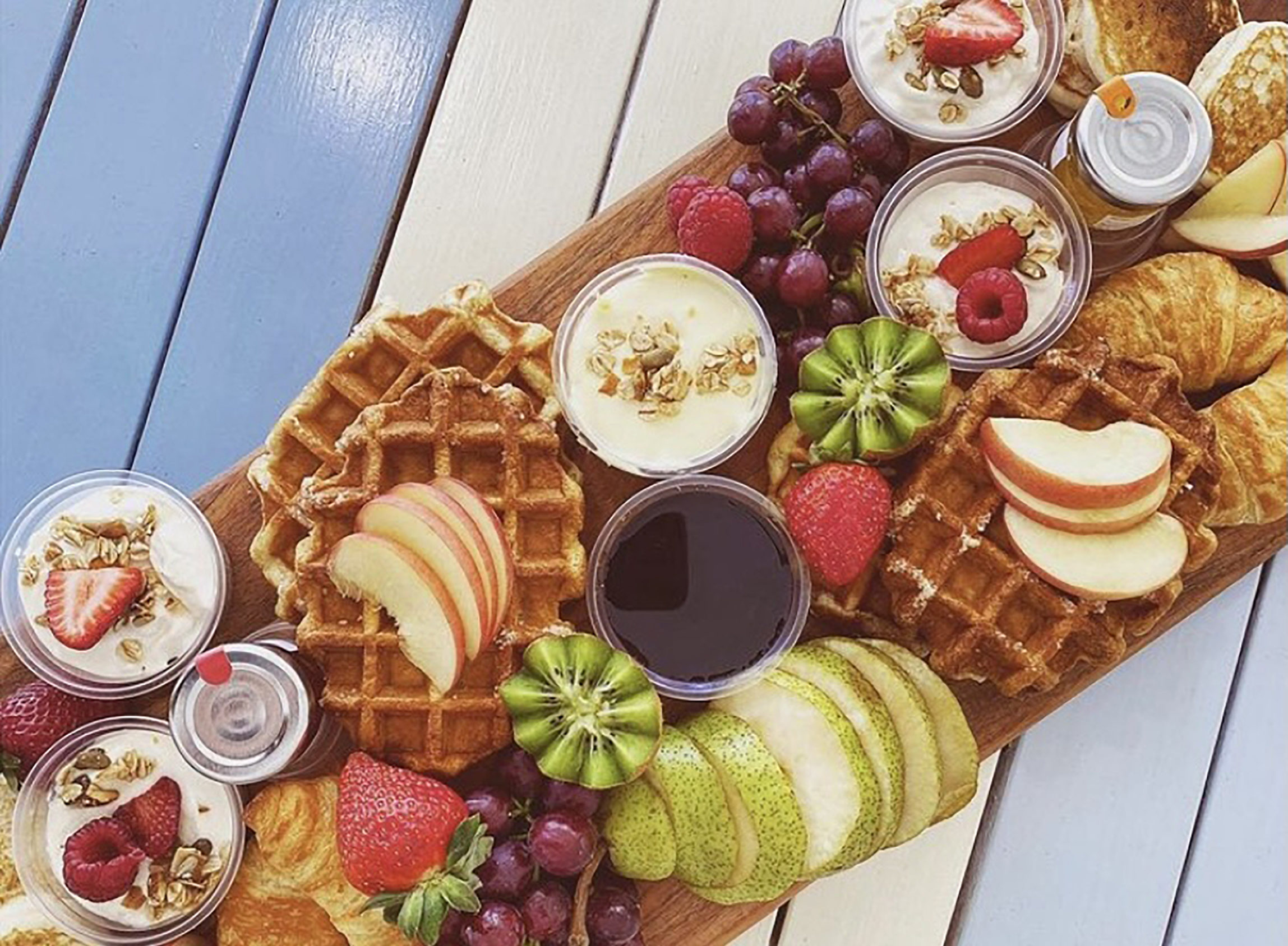 a colourful platter of breakfast food including waffles fruit and yoghurt on a blue and white striped table
