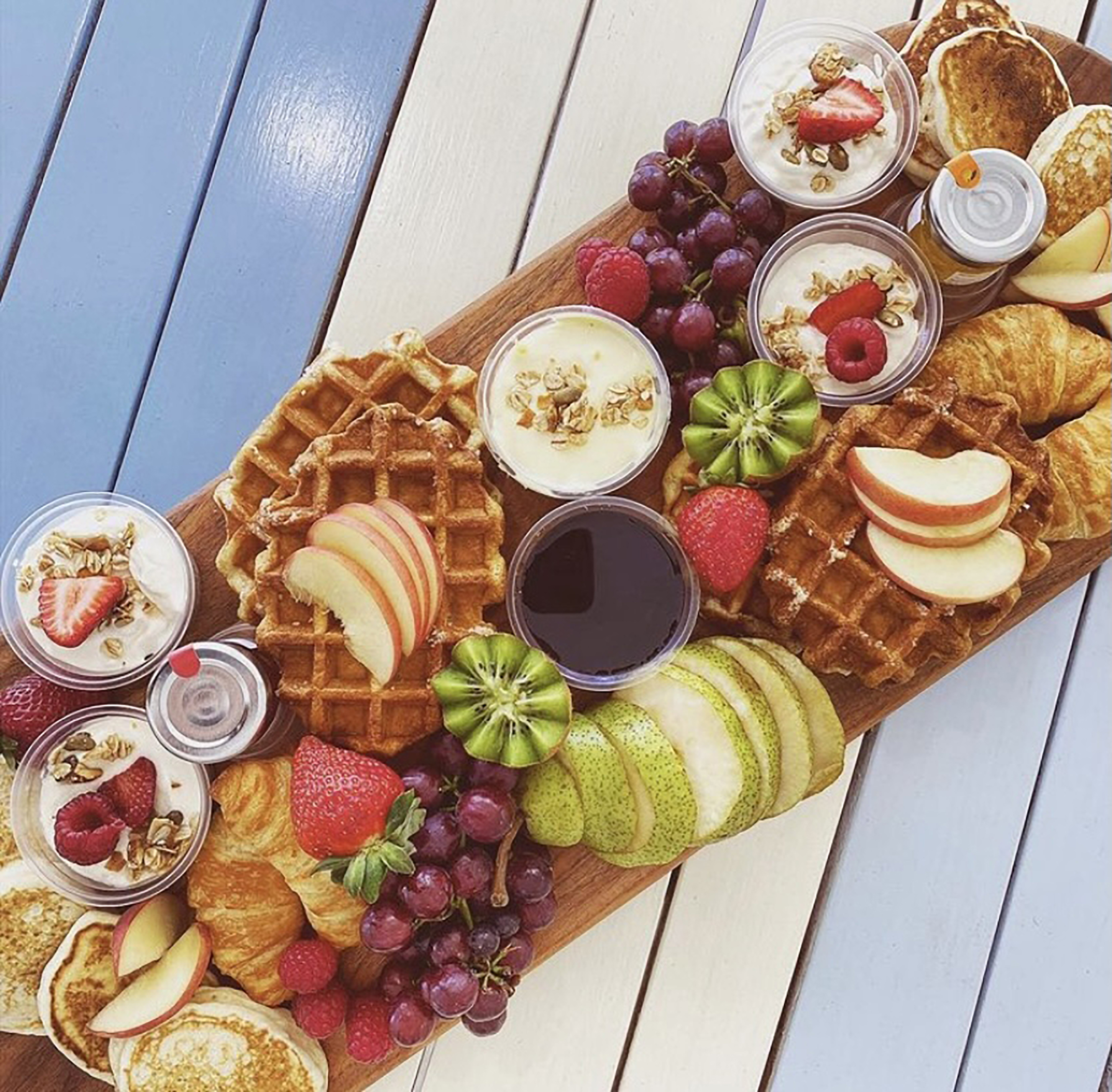 a colourful platter of breakfast food including waffles fruit and yoghurt on a blue and white striped table