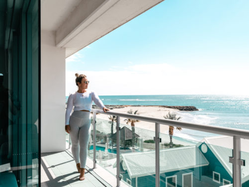 Girl on Seashells Mandurah balcony in Pilates clothes with view of swimming pool and ocean in the background